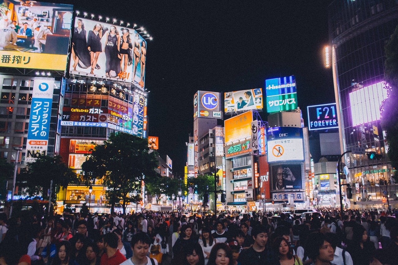 Shibuya crossing at night, one of the busiest intersections in Tokyo, lined by tall buildings with large billboard advertisements and bright neon lights.